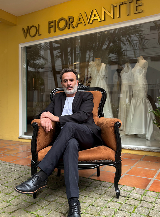 Estilista Vol Fioravante sentado em poltrona na fachada do ateliê em Balneário Camboriú